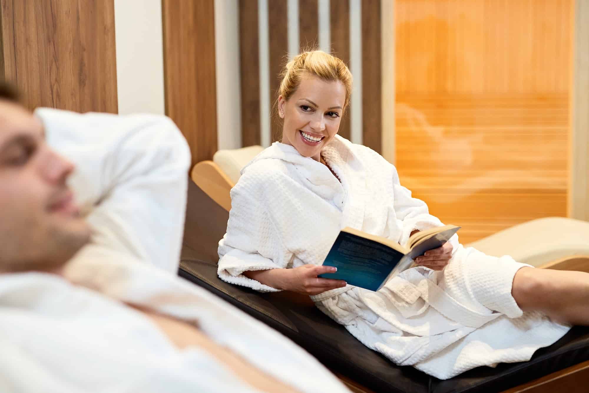 Happy woman in bathrobe reading a book at the spa.