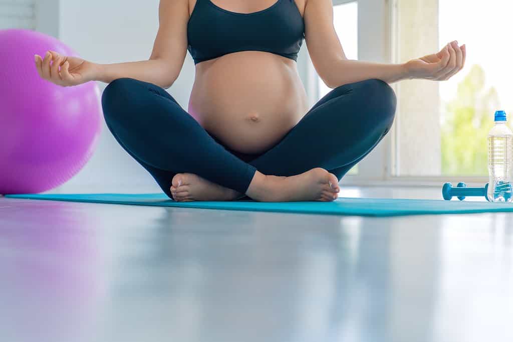 Cropped shot of pregnant woman doing yoga meditation at home